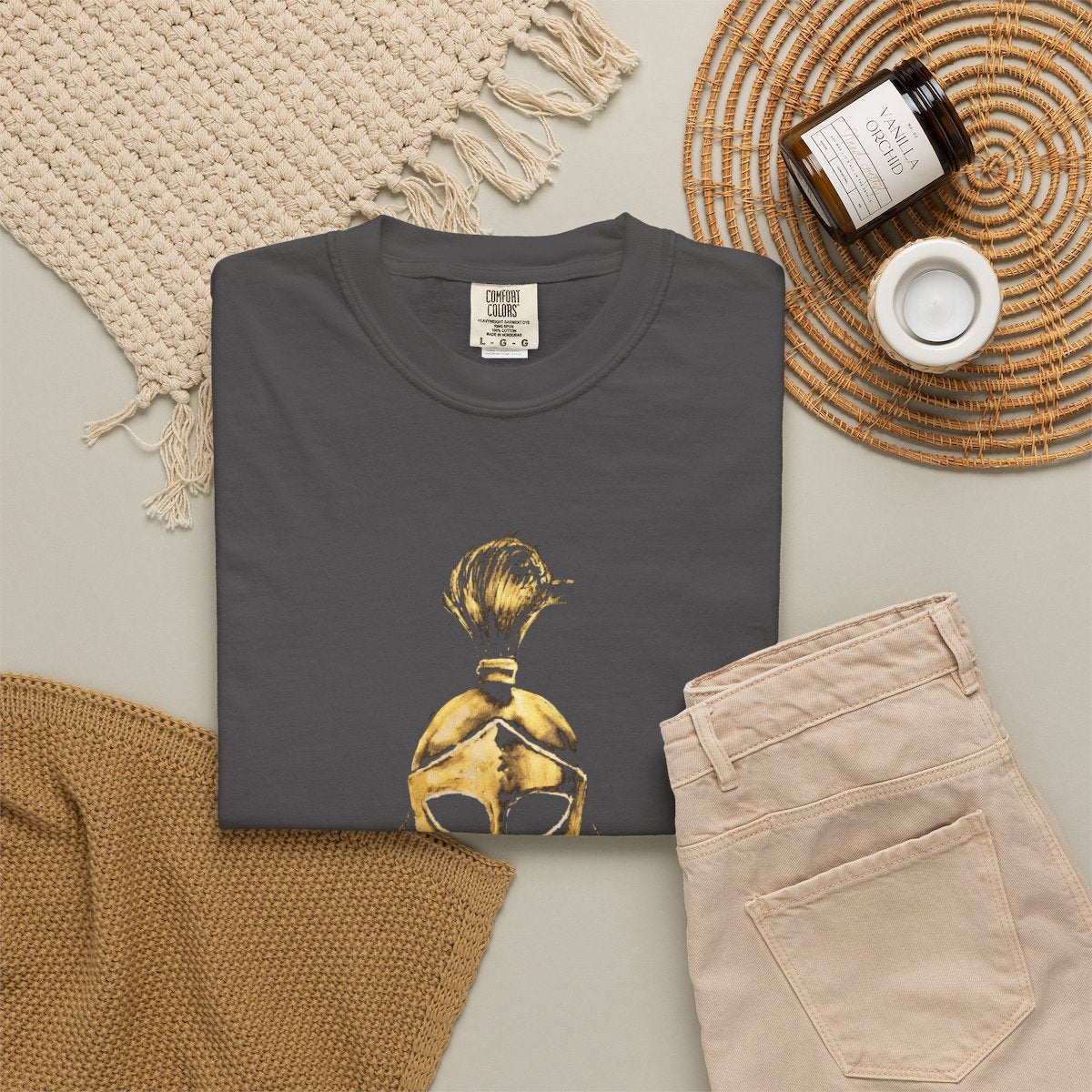 Graphite casual tee folded in a flat-lay, gold Sentinel helmet on the front
